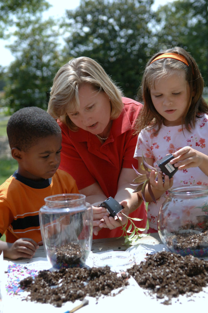 A volunteer works with students to make terrariums,